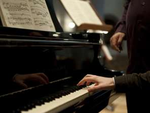 Ein Klavier mit Musiknoten. Eine Person spielt mit einer Hand.