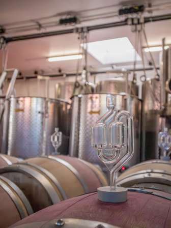 Weinkeller Hallau Ein Gärspund steckt in einem Holzfass. Im Hintergrund stehen mehrere Stahltänke.