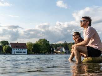 Zwei Personen sitzen auf grossen Steinen im Rhein und kühlen die Füsse im Wasser ab.