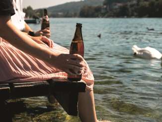 Biergenuss am Rhein Zwei Freundinnen sitzen an einem Holzsteg und lassen die Füsse im Rhein baumeln. In der Hand haben sie eine Flasche Bier. Es schwimmt ein Schwan vorbei.