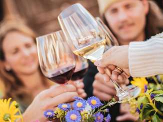 Vier Personen stossen mit einem Glas Wein an. Blumendekoration steht auf dem Tisch.