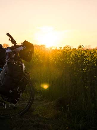Fahrrad mit Gepäck Ein bepacktes Fahrrad steht vor einem leuchtend gelben Rapsfeld, warmes Abendlicht taucht die Szene in goldene Farbtöne.