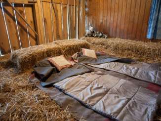 In einem Strohraum liegen auf zwei Wolldecken mit Kissen und Decken als Bett.