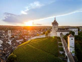 Blick auf die Rundfestung Munot mit Reben. Dahinter sieht man die Schaffhauser Altstadt. Hinter dem Hügel geht die Sonne unter.