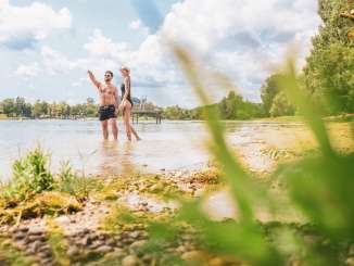 Strandbad Stein am Rhein Zwei Personen stehen in Bademode im Rhein an einem Sandstrand.