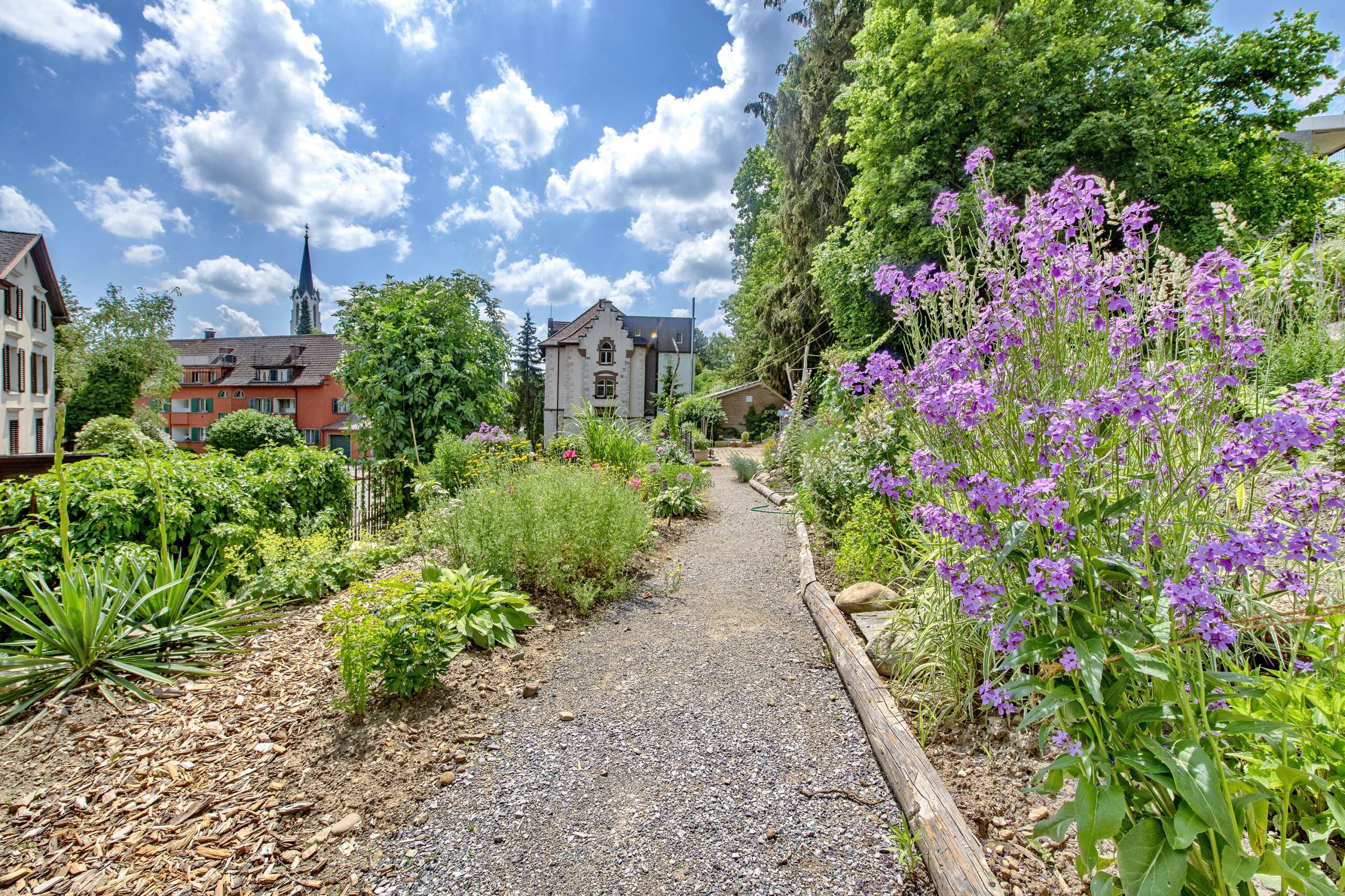 Zu einem Hotel gehörende Parkanlage mit bunten Blumen, blauem Himmel.