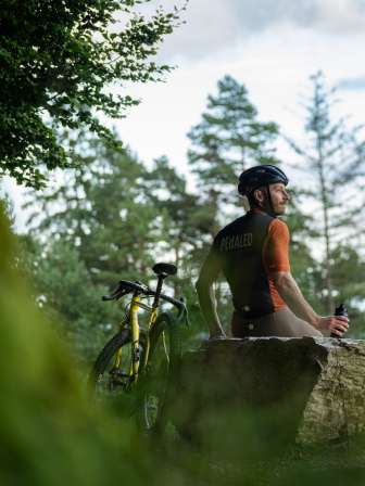 Ein Velofahrer sitzt auf einem grossen Stein und macht eine Pause auf seiner Graveltour.