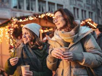 Zwei Frauen mit einem Becher Glühwein in der Hand an einem Weihnachtsmarkt.