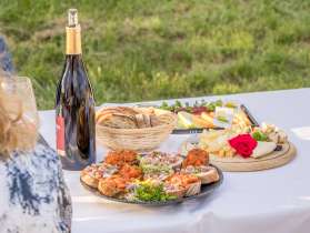 Vorspeise Catering Schaffhauser Tavoalata Auf einem Tisch mit weisser Tischdecke draussen stehen Platten mit verschiedenen Vorspeisen. Es hat eine Platte mit Käse, eine mit Broten mit Belag und eine mit Melonen.