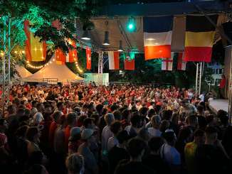 Viele Fussballfans sitzen im einem Park und schauen ein Fussballspiel auf einer grossen Leinwand.