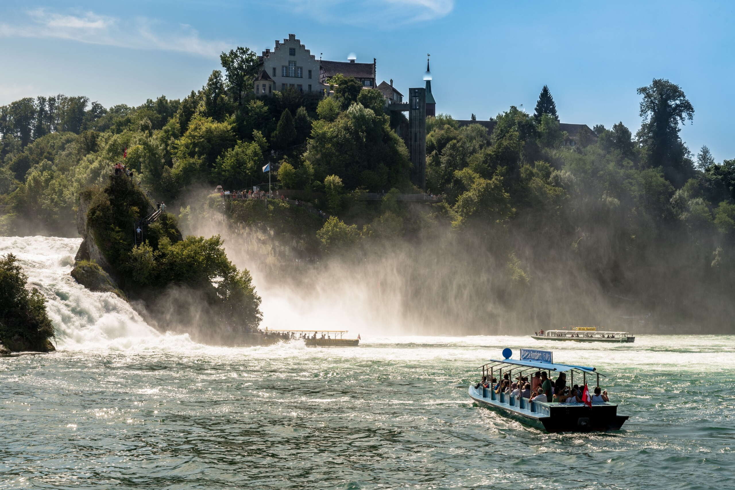 Drei Boote fahren im Rheinfallbecken. Im Hintergrund ist das Schloss Laufen.