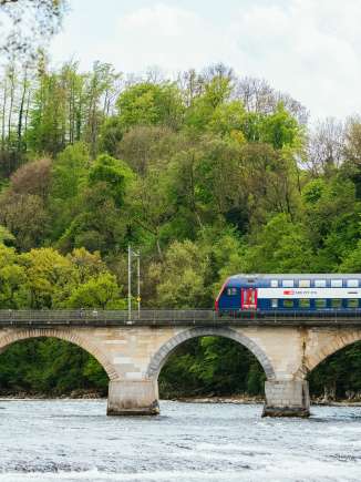 rheinfall-bruecke-zug-april-fruehling Ein Zug der SBB fährt vom rechten Bildrand über die Rheinfall Brücke.