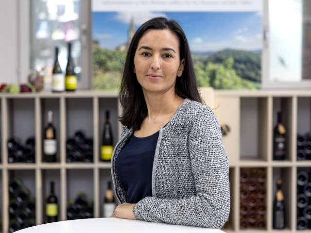 Portrait Tugba Özer. Sie hat schwarze Haare und trägt ein dunkel blaues T-Shirt und ein weiss graues Jäckli.