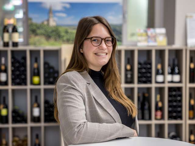 Amanda Suter hat braune Haare, trägt einen karierten Blazer, ein schwarzer Oberteil und eine Brille.