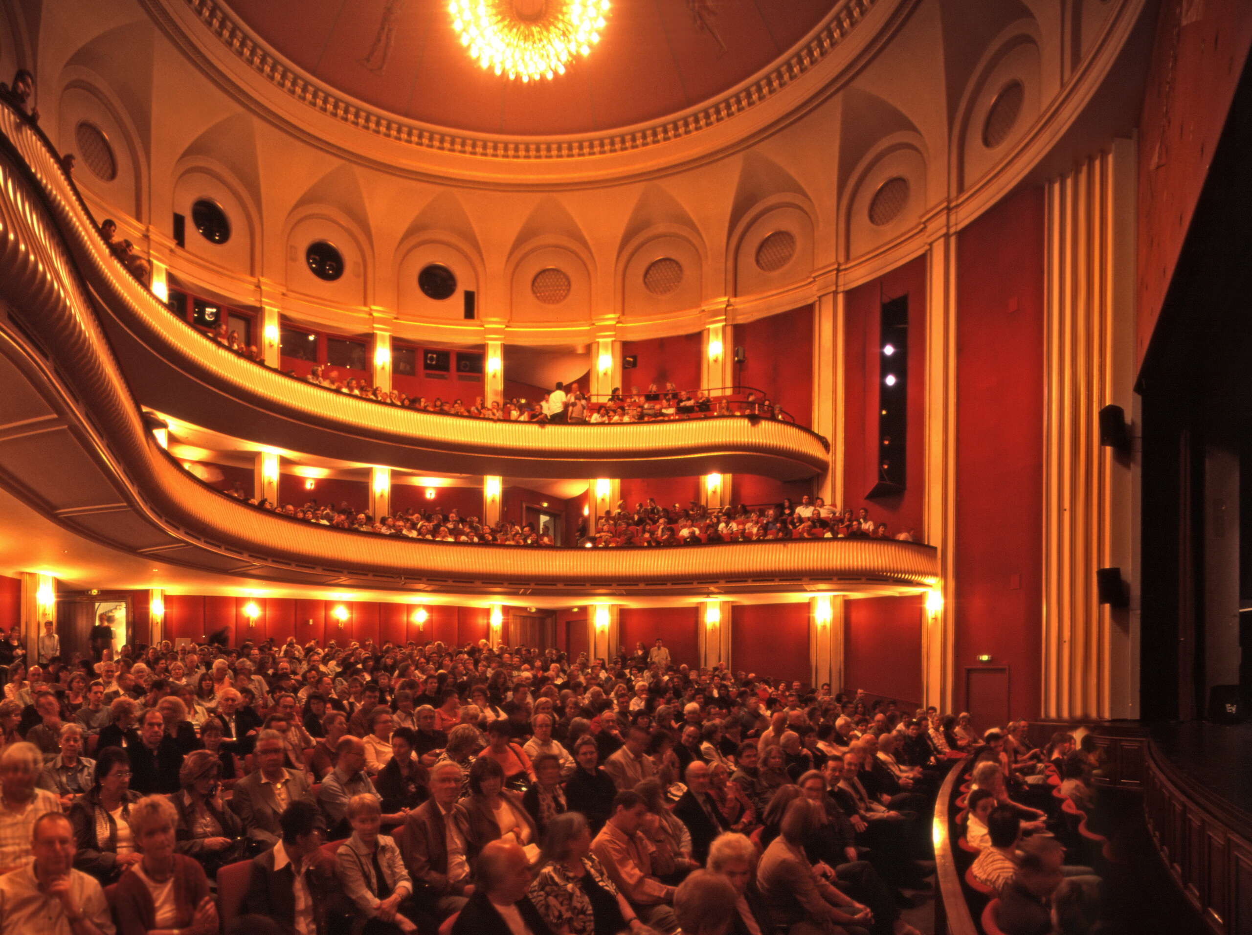 Blick auf das Publikum und die Galerien im Stadttheater Schaffhausen Von der Decke hängt ein grosser Kronleuchter.