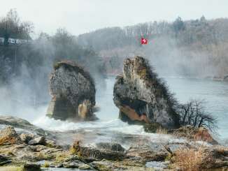 Der Rheinfall Mittelfelsen im Winter mit Nebel. Auf dem Felsen weht eine schweizer Fahne.
