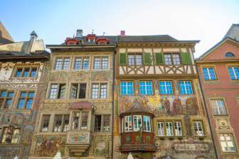 Vier Häuser mit alten bemalten Fassaden. Ebenfalls sind zwei Erker zu sehen, welche hervorstehen.