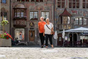 Zwei Personen laufen über den rathausplatz Stein am Rhein. Im Hintergrund sind die weltberühmten Fassadenmalereien.