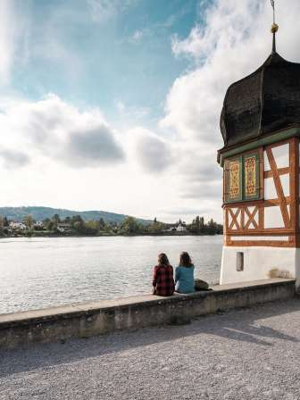 Stein am Rhein Wanderpause Zwei Freundinnen sitzen am Rheinufer und machen eine Pause. Links neben Ihnen steht ein kleiner Riegel-Turm mit Zwiebeldach.