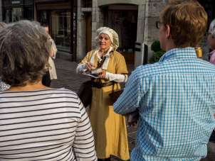 Führung «Mittelalterliche Gerüche» Ein Guide verkleidet in einem gelben Gewand und einer Haube steht vor eine Gruppe.