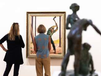 Zwei Frauen stehen vor einem Bild, auf dem ein Mann mit einer Axt einen Baum fällt.