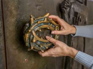 Stadtführun gfür Sehbeeinträchtigte Zwei Hände ertasten einen Türgriff einer Kirche. Der Griff ist ein Rosenkranz mit Dornen.
