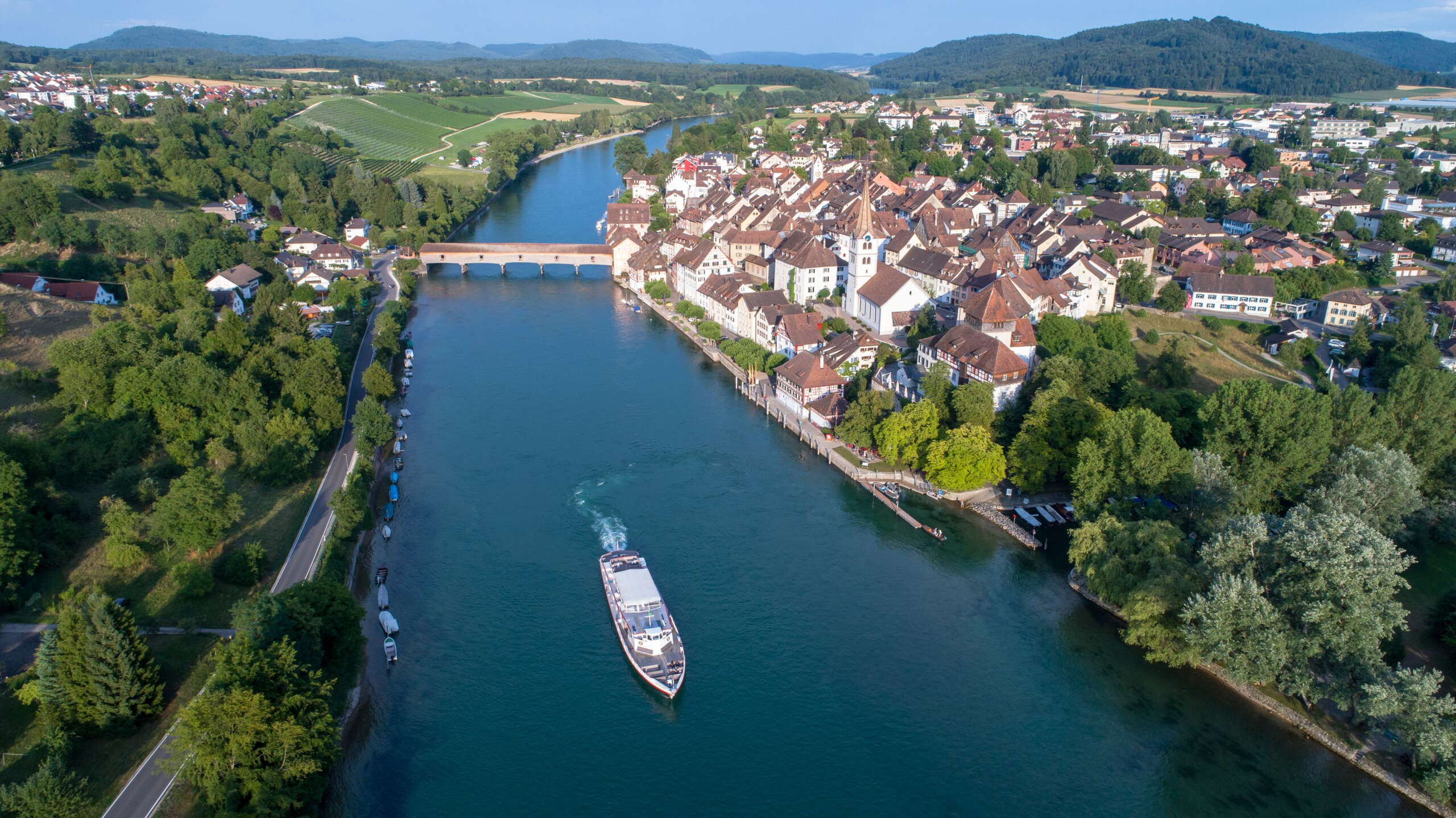 Blick von oben auf den Rhein, wo ein Kursschiff fährt und das Städtchen Diessenhofen im Hintergrund.