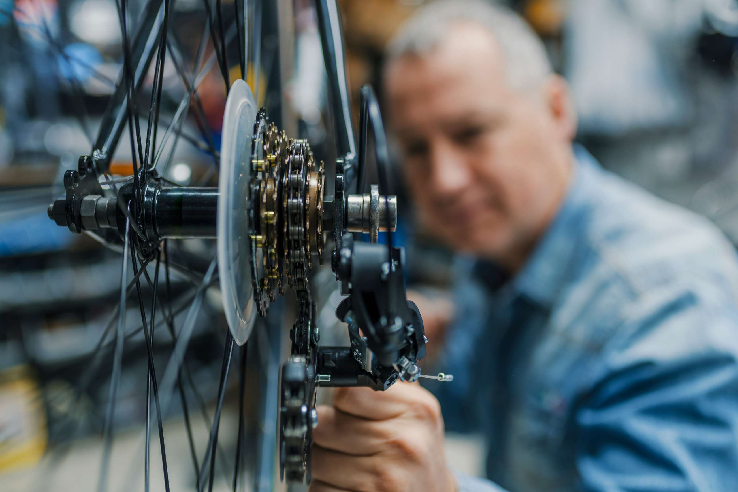 Ein Mann führt eine Reparatur am Hinterrad eines Fahrrads durch, sichtbar sind Speichen, Kette und Teil des Rahmens.