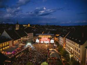 Ein Platz zwischen Häuser in der Altstadt. Der Platz ist gefüllt mit Menschen. Vorne Befindet sich eine Bühne mit der Aufschrift "Stars in Town".