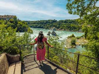 Touristin am Rheinfall Eine Touristin trägt ein sommerliches Kleid und steht an einem Aussichtspunkt und schaut auf den Rheinfall.