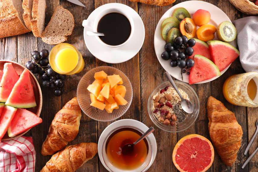 Holztisch mit Früchten, Kaffee, Gipfeli, Müesli und Brot.