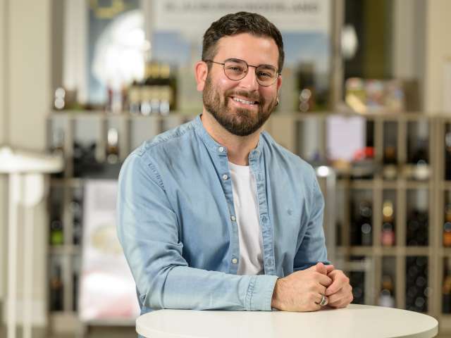 Portrait Patrick Pozas. Er hat schwarze Haare und Bart, trägt eine Brille und hat ein blaues Jeanshemd an mit weissen T-Shirt.