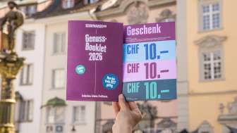 Eine Person hält das Genuss-Booklet in die Luft. Eine Broschüre mit Genusstipps und Gutscheinen zum Einlösen.