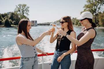 Drei Freundinnen stossen mit einem Glas Wein auf einem Schiff an.