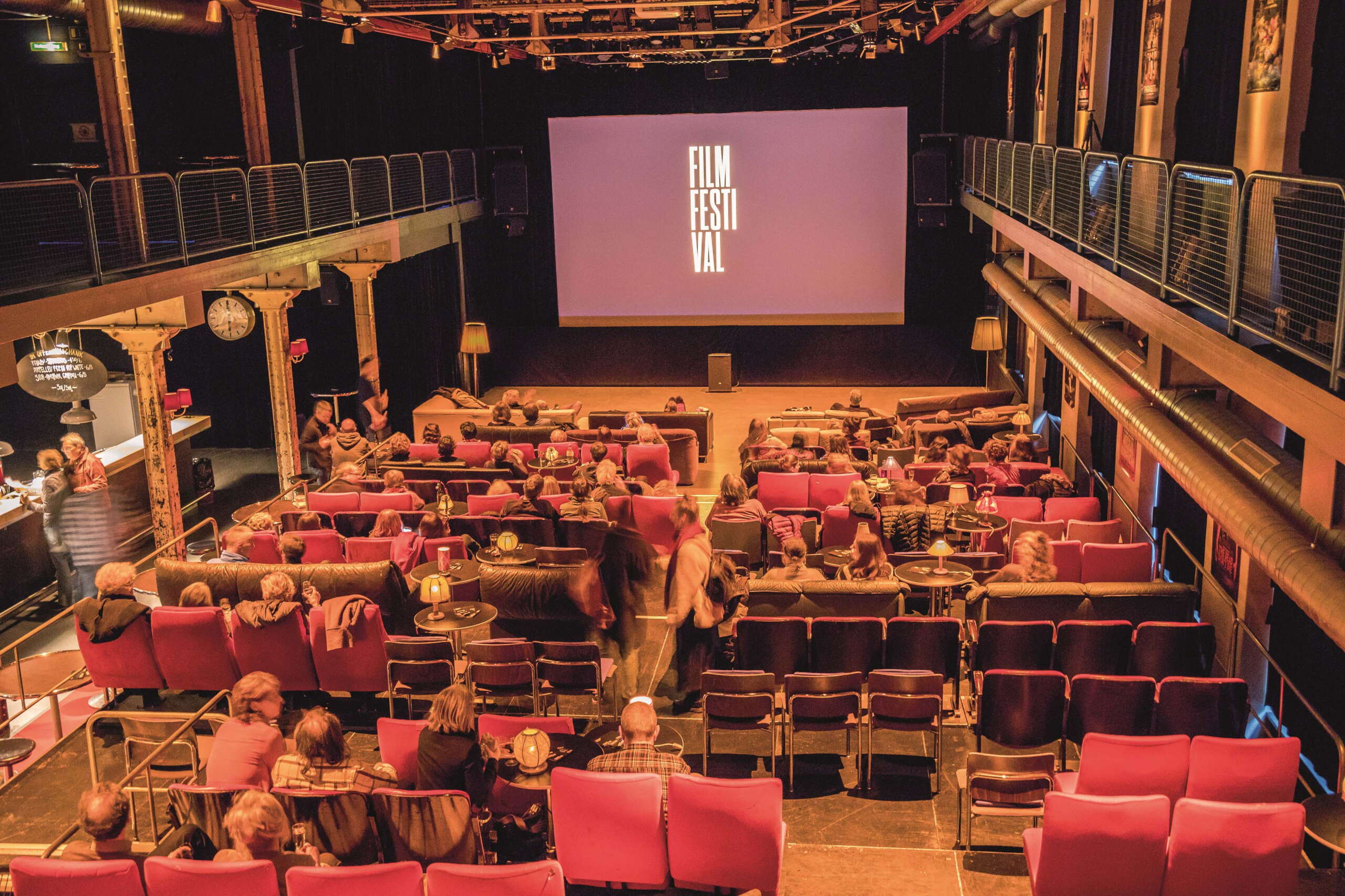 Ein Kino in einer alten Fabrikhalle mit grosser Leinwand und roten Sesseln.