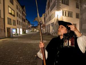 SteinamRhein_Nachtwaechter_Altstadt Es ist die Abenddämmerung in Stein am Rhein. Eine als Nachtwächter verkleidete Person steht mitten in der Altstadt Stein am Rhein. In der einen Hand eine Laterne und in der anderen eine Hellebarde.