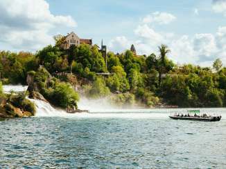Bootsfahrt am Rheinfall Ein grünes Boot fährt im Rheinfallbecken auf den Wasserfall zu. An Bord sind viele Personen.