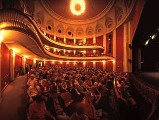 Das Stadttheater mit dem Parterre und zwei Balkonen ist gefüllt mit Zuschauenden.