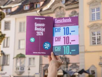 Eine Person hält das Genuss-Booklet in die Luft. Eine Broschüre mit Genusstipps und Gutscheinen zum Einlösen.