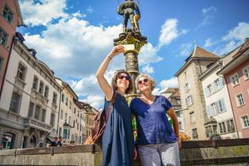 Zwei Frauen stehen vor einem Brunnen in der Schaffhauser Altstadt und machen ein Selfie.