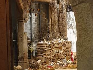 Blick auf einen weihnachtlich geschmückten Eingangsbereich mit Holzstapel, Holsternen und Weihnachtskugeln.
