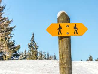 Ein gelber Wander-Wegweiser auf einem schneebedecktem Feld.