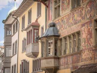 Blick auf mehrere Häuserfassaden mit einem Erker. Eine Fassade ist leicht gelb, die andere reich mit Malereien verziert.