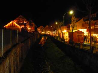 An einer Strasse entlang eines Baches stehen diverse beleuchtete Markstände.