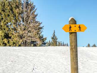 Ein oranger Wander-Wegweiser auf einem schneebedecktem Feld.
