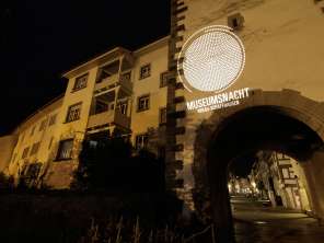 Eine alte Stadtfassade mit Torbogen in der Nacht. Die Fassade wird beleuchtet mit dem Slogan "Museumsnacht Hegau-Schaffhausen.