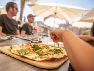 Flammkuchen essen auf Terrasse Auf einer Restaurantsterrasse auf einem Tischt steht ein Flammkuchen mit bunten Gemüse.