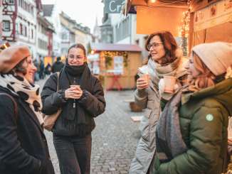 Vier Frauen an einem Weihnachtsmarkt mit einem Becher Glühwein in der Hand.