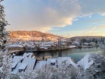 Ein Mittelalterliche Stadt, wo ein Fluss mitten durch fliesst. Die Hausdächer sind mit Schnee bedeckt.