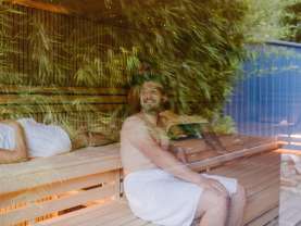 Personen sitzen in einer Sauna. Im Glas spiegeln sich Bambusblätter.
